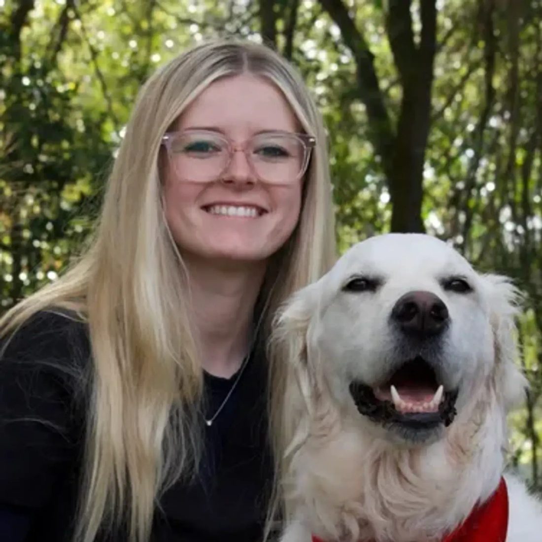 Blonde woman with glasses posing with a golden retriever outdoors