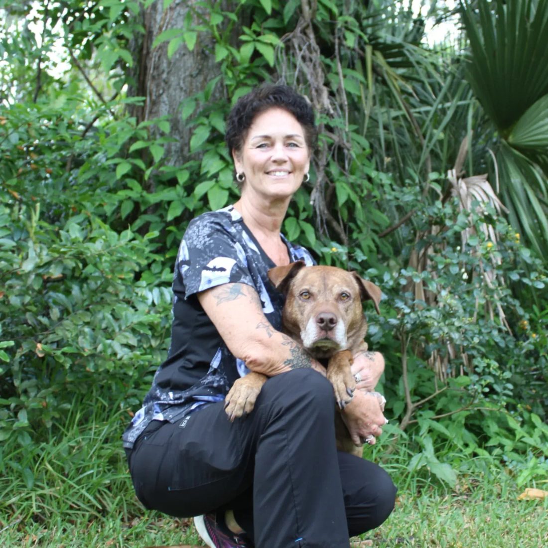 Woman crouching with a brown dog in a lush garden setting